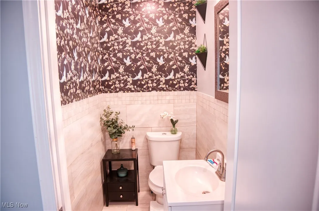 Half bathroom featuring vanity, tile walls, a wainscoted wall, wallpapered walls, and tile patterned floors