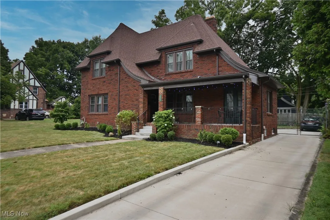 View of front of house featuring a front lawn, covered porch, brick siding, and chimney