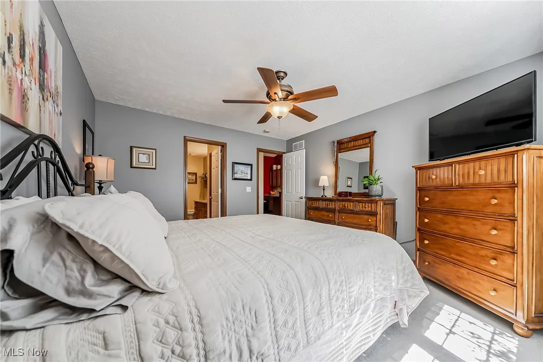 Bedroom featuring ceiling fan, carpet flooring, ensuite bath, and a textured ceiling