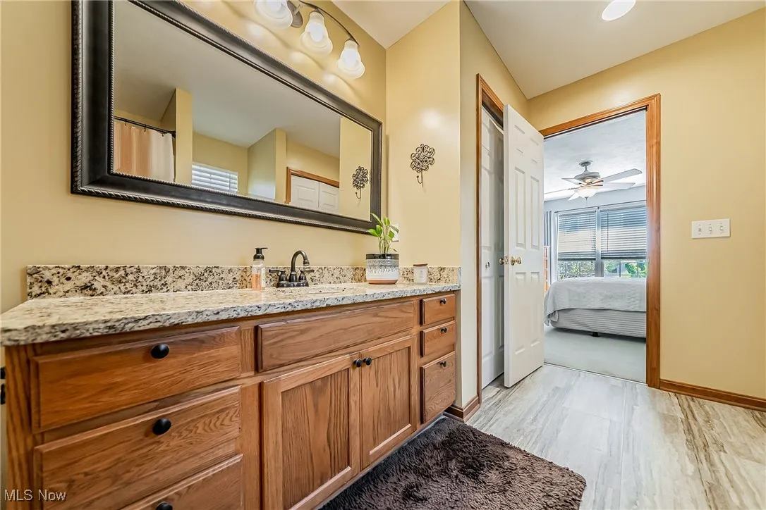 Ensuite bathroom with vanity, light wood-style flooring, and ceiling fan