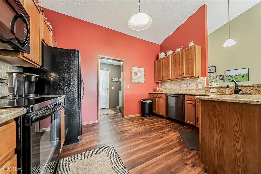Kitchen featuring decorative backsplash, brown cabinets, black appliances, light stone counters, and dark wood finished floors