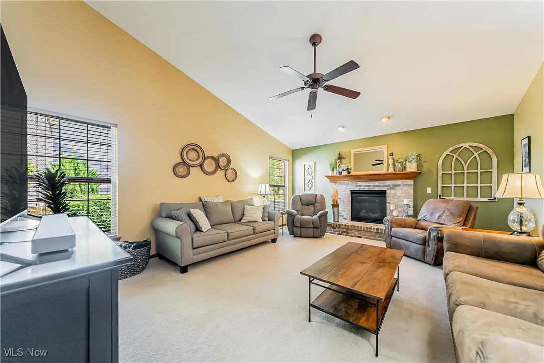Living area with light carpet, a brick fireplace, a ceiling fan, and high vaulted ceiling