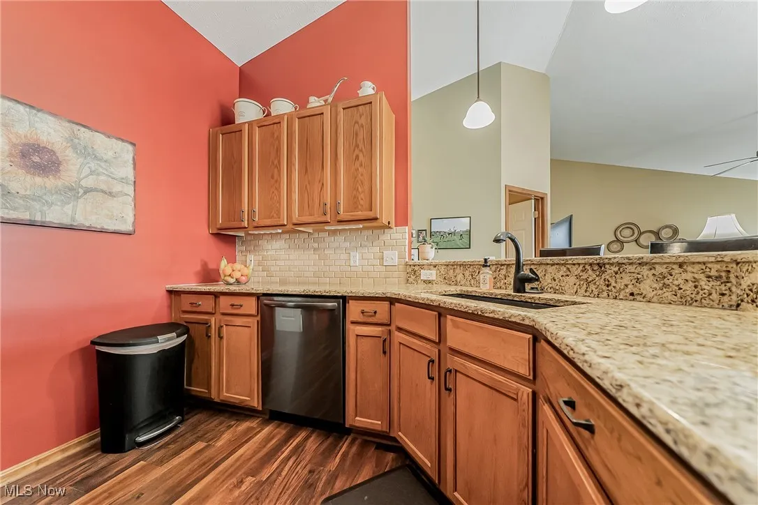 Kitchen with brown cabinets, stainless steel dishwasher, tasteful backsplash, and light stone countertops