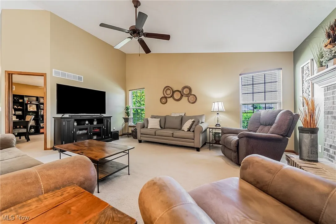 Living area with light carpet, ceiling fan, and high vaulted ceiling