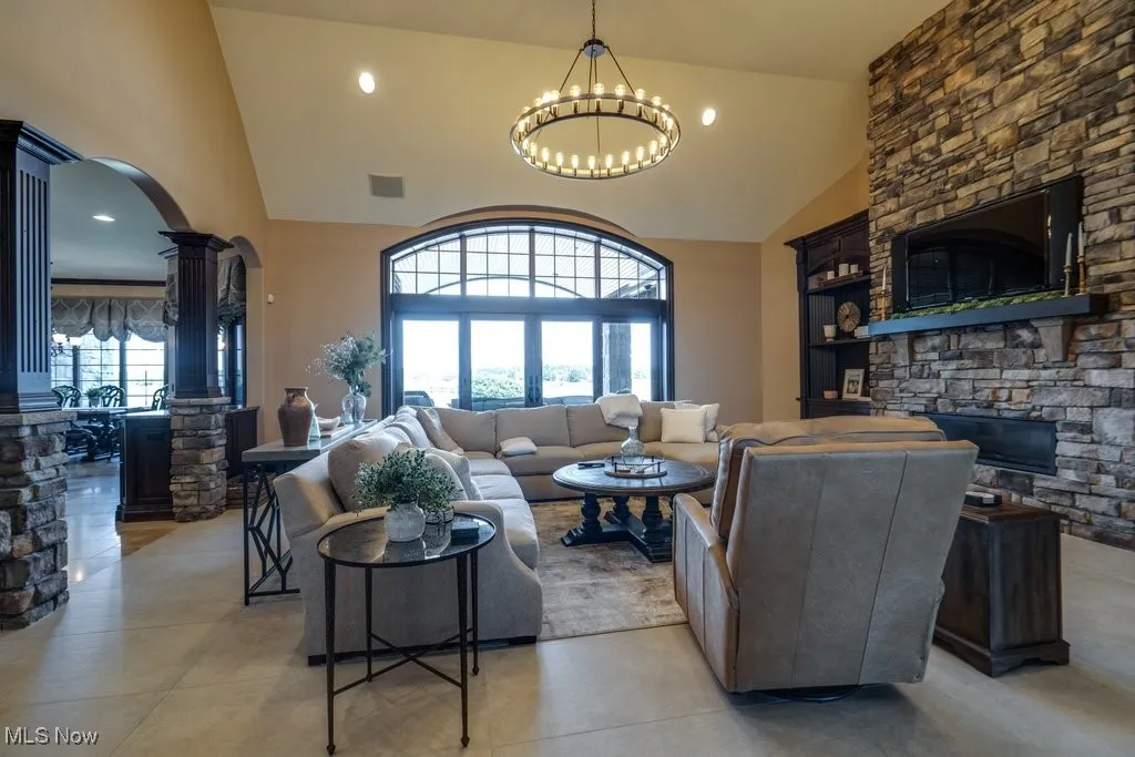Living area with a stone fireplace, arched walkways, high vaulted ceiling, decorative columns, and recessed lighting