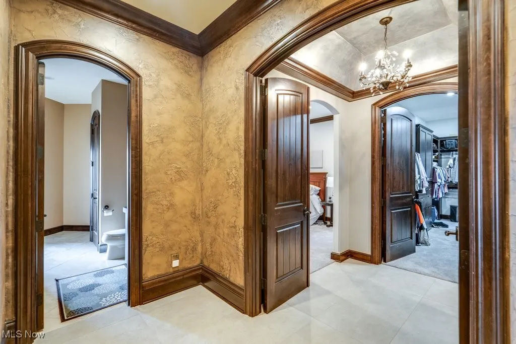 Hall featuring ornamental molding, arched walkways, a chandelier, and light tile patterned floors
