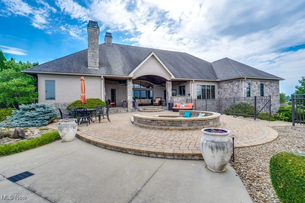 Rear view of property with a patio, a chimney, stone siding, a shingled roof, and stucco siding