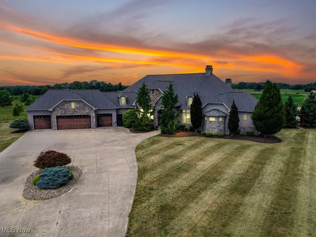 French country inspired facade featuring stone siding, driveway, a chimney, an attached garage, and a front yard