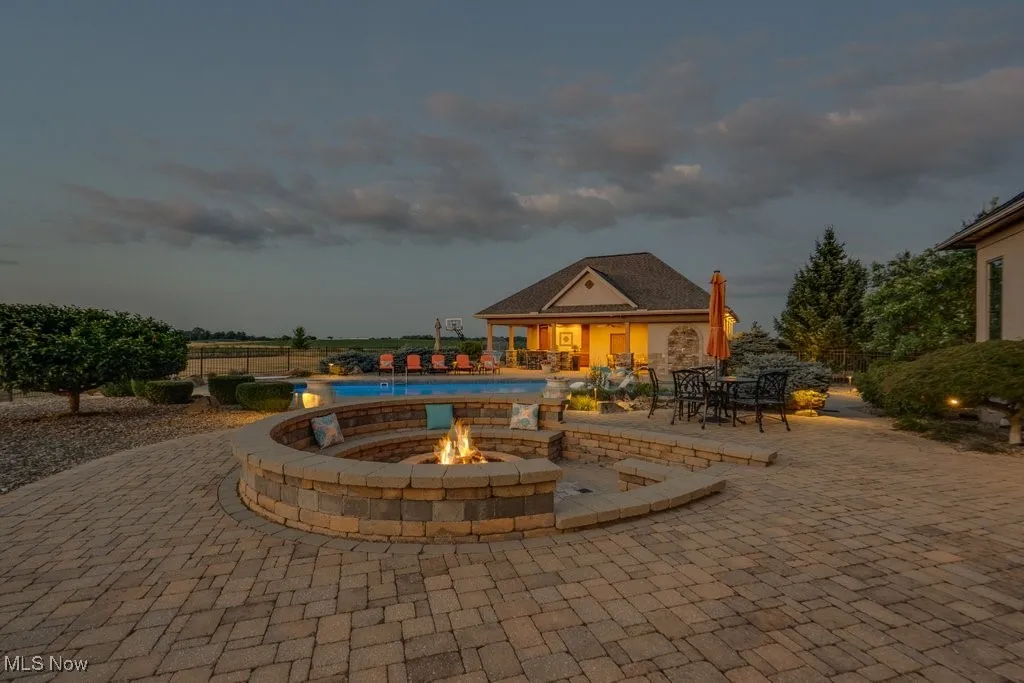 Pool at dusk with a patio area, a fire pit, and an outdoor structure