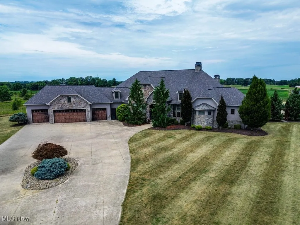 View of front of home with stone siding, a chimney, driveway, and a garage