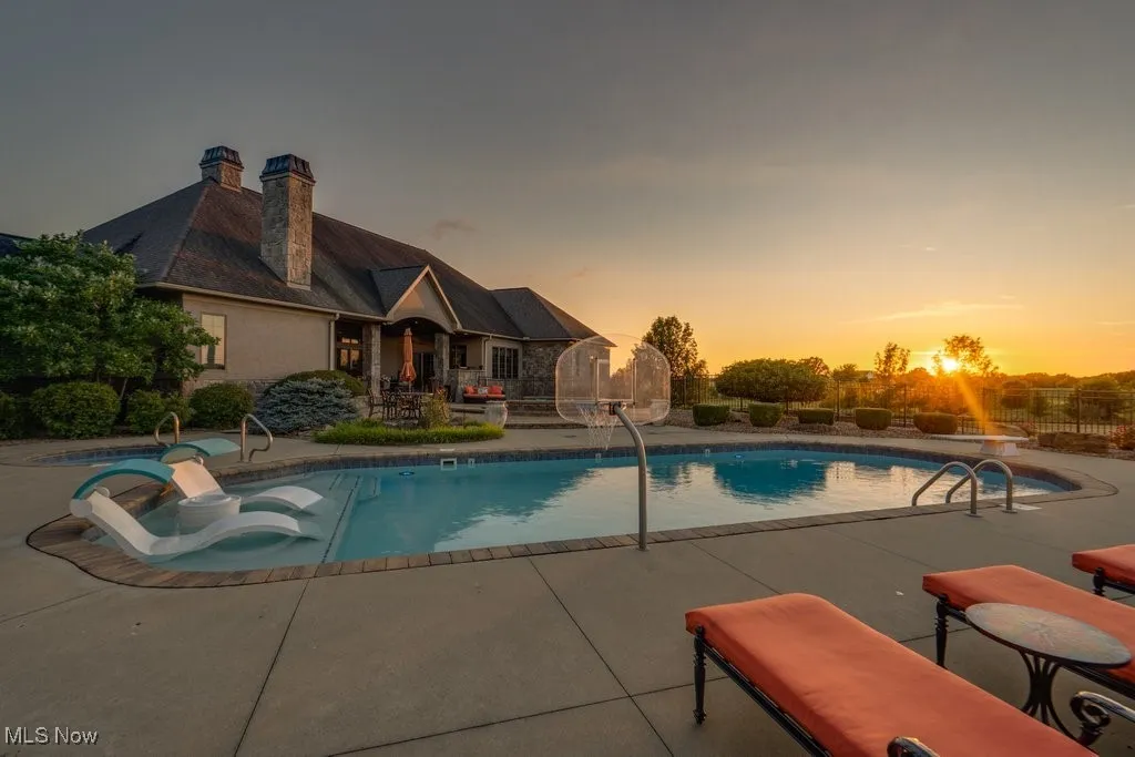 Pool at dusk featuring a patio and a hot tub