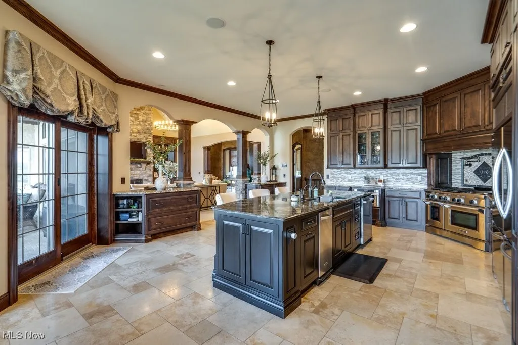 Kitchen featuring arched walkways, decorative backsplash, glass insert cabinets, decorative light fixtures, and crown molding