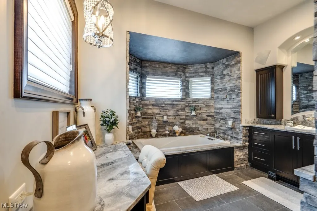 Full bath with vanity, a bath, dark tile patterned flooring, and a chandelier