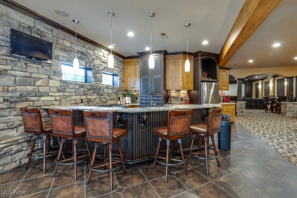 Bar featuring light stone counters, crown molding, pendant lighting, freestanding refrigerator, and recessed lighting