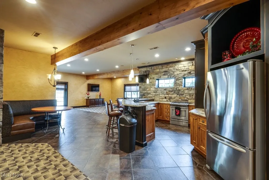Kitchen with beamed ceiling, appliances with stainless steel finishes, light stone counters, hanging light fixtures, and recessed lighting