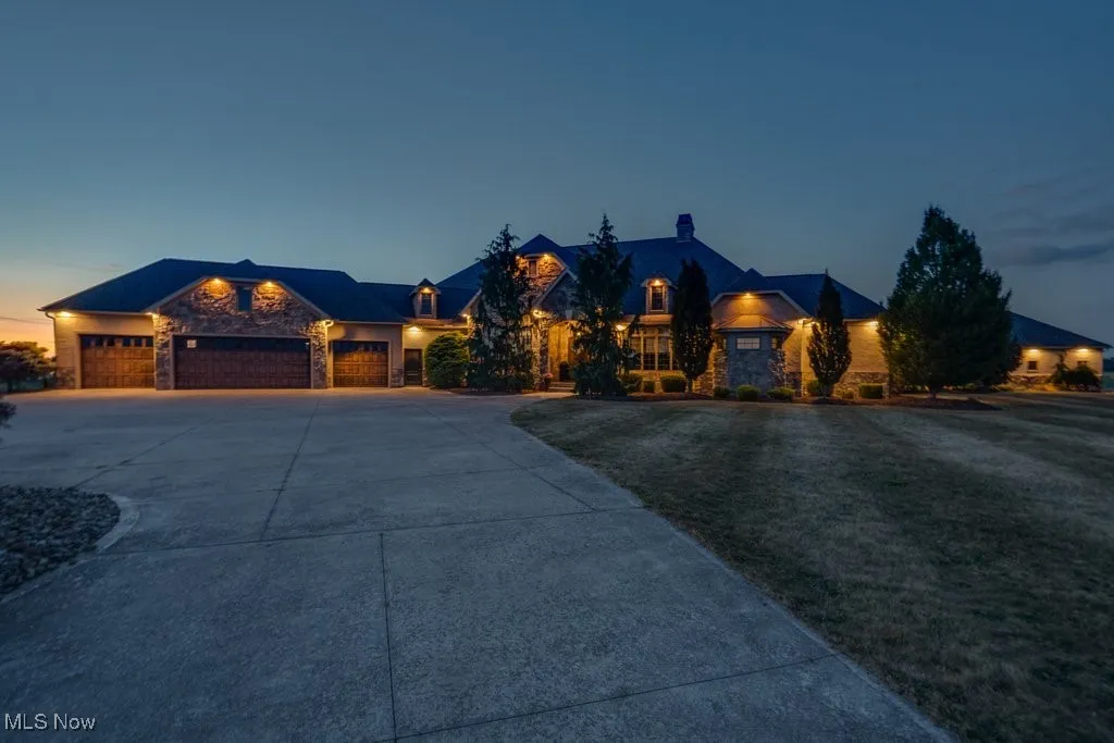 View of front of house featuring stone siding, concrete driveway, an attached garage, and a chimney