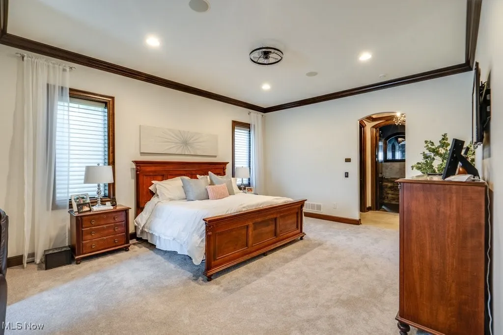 Bedroom with ornamental molding, light colored carpet, arched walkways, multiple windows, and recessed lighting
