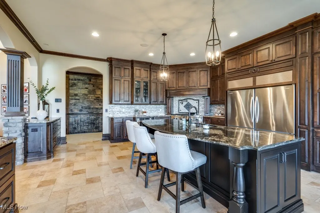 Kitchen featuring a breakfast bar area, glass insert cabinets, dark stone counters, arched walkways, and ornamental molding