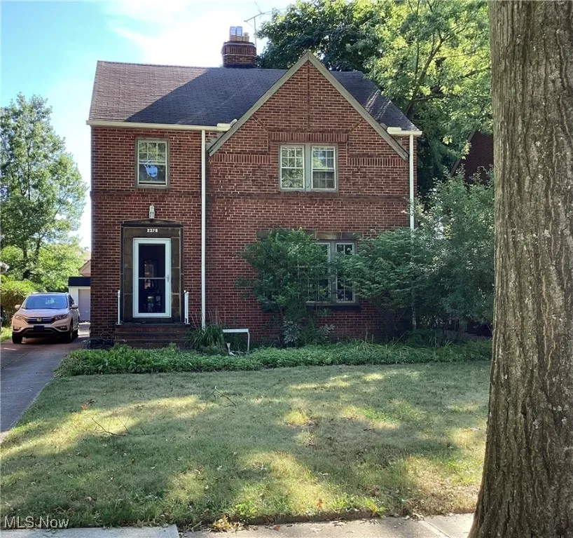 View of front facade with brick siding, a chimney, a front yard, and a shingled roof