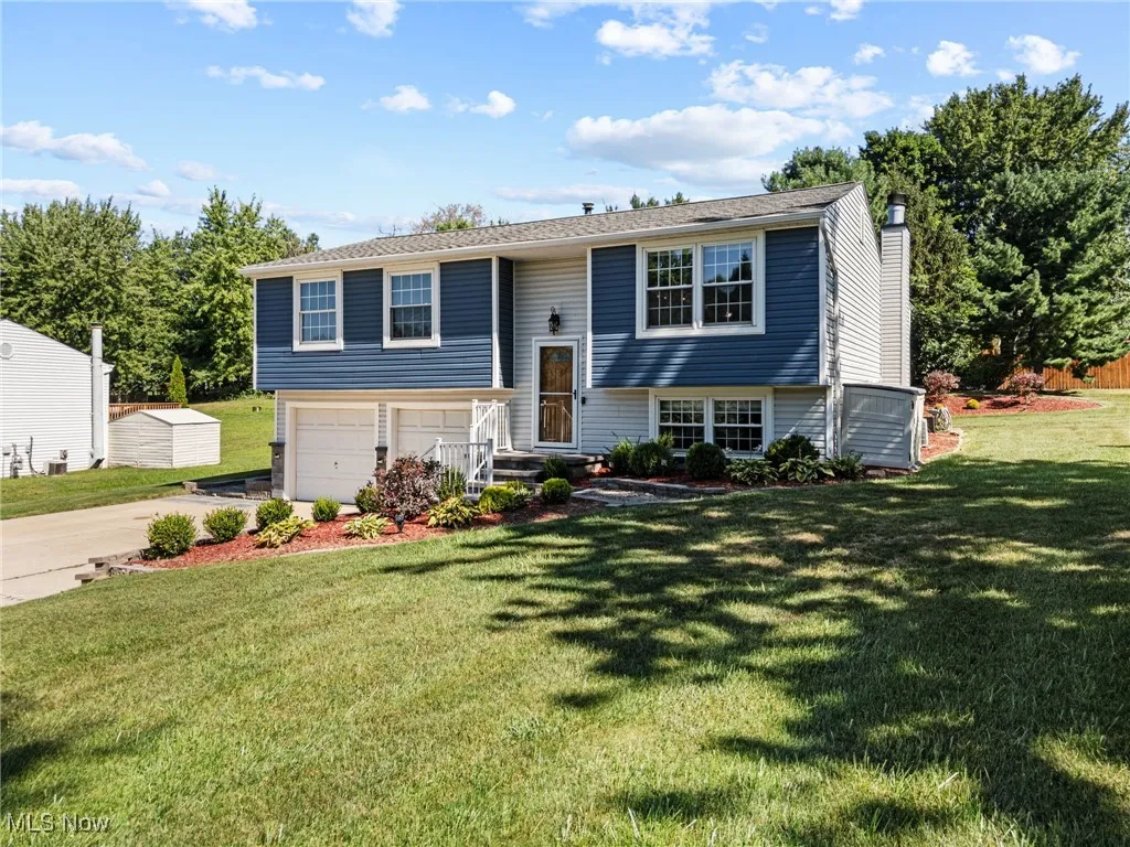 Bi-level home with an attached garage, concrete driveway, a chimney, and a front yard