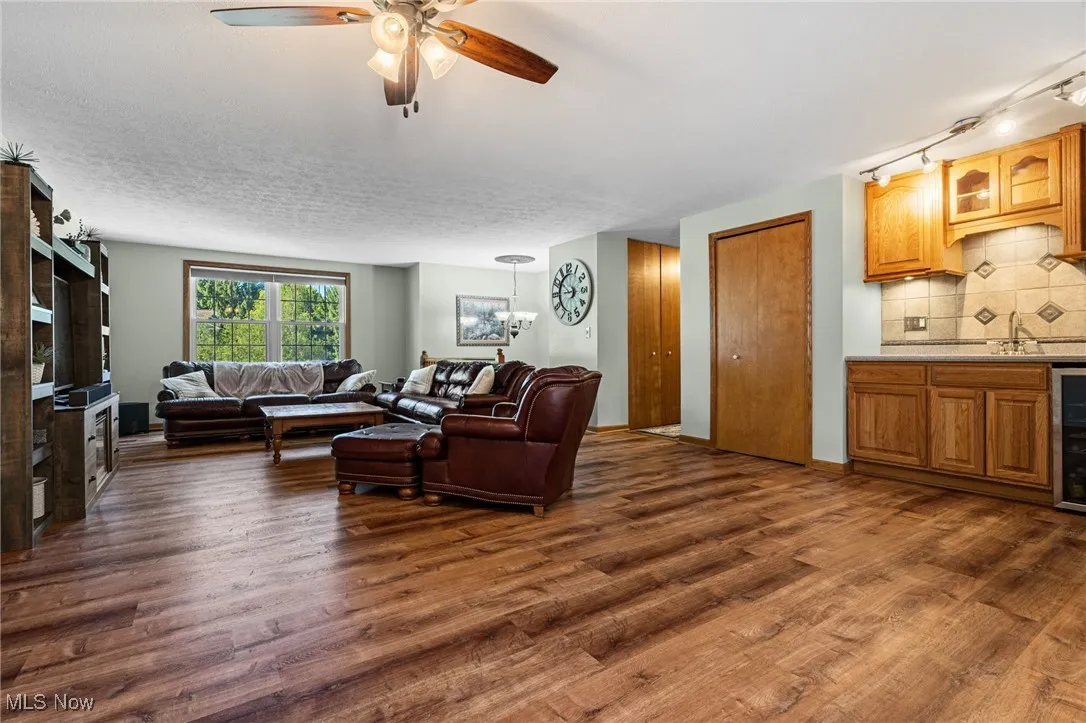 Living room with dark wood-style flooring, ceiling fan, and beverage cooler
