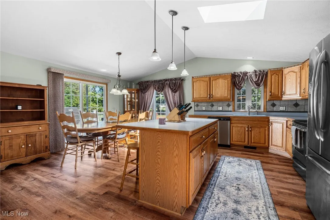 Kitchen featuring brown cabinets, backsplash, light countertops, appliances with stainless steel finishes, and pendant lighting