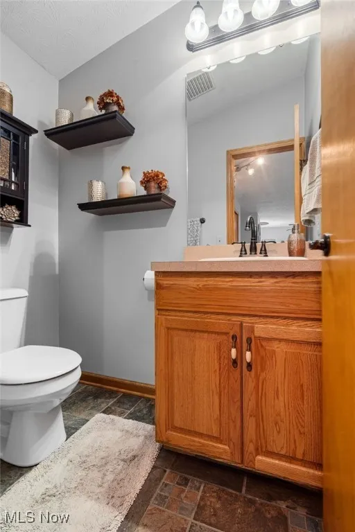 Half bath with vanity, stone tile floors, and a textured ceiling