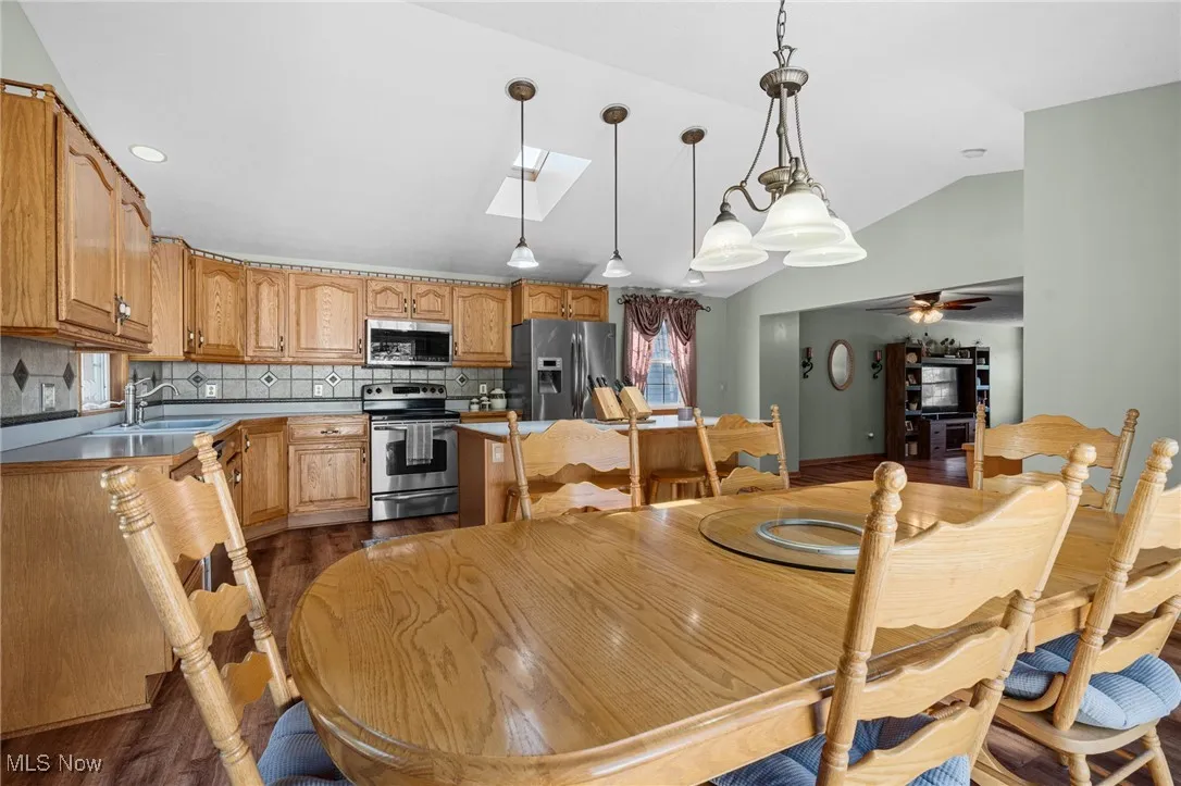Dining room featuring dark wood finished floors, vaulted ceiling, a skylight, and a ceiling fan