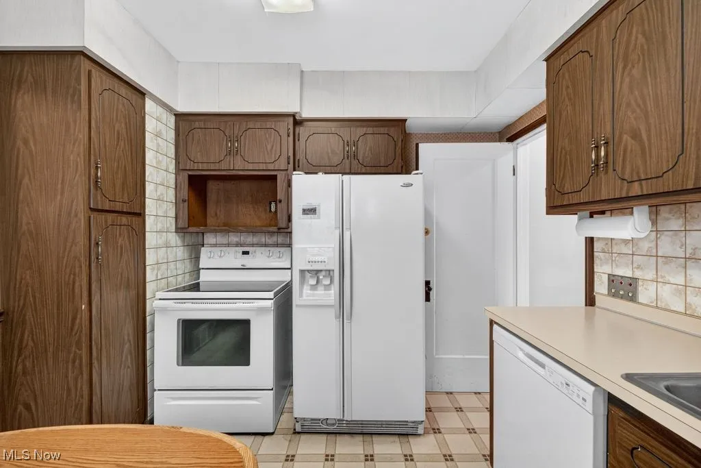 First Floor kitchen featuring white appliances, backsplash, light countertops, light floors, and brown cabinetry
