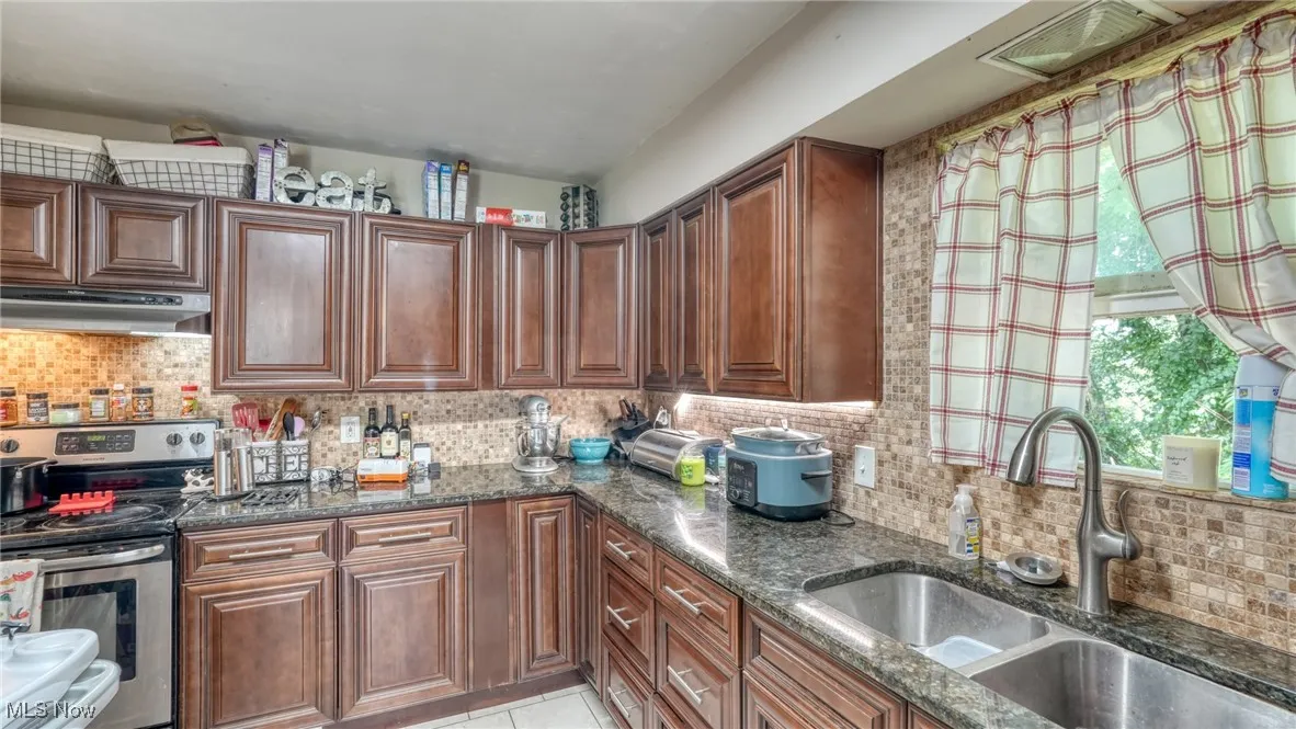 Kitchen featuring backsplash, electric stove, dark stone counters, and under cabinet range hood