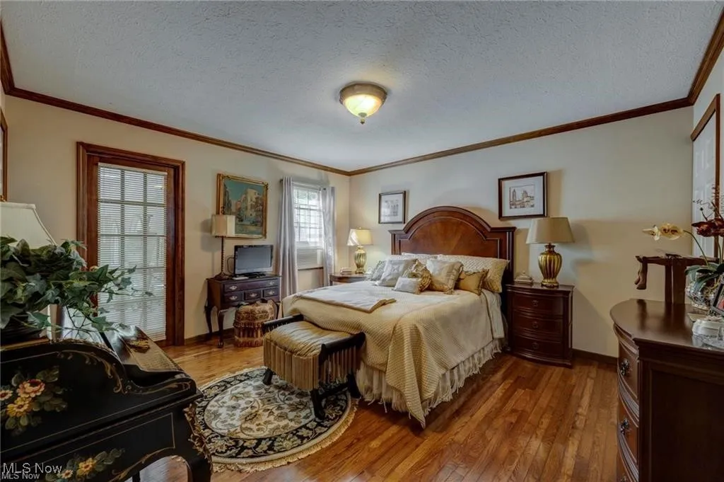 Bedroom with a textured ceiling, hardwood / wood-style floors, and ornamental molding