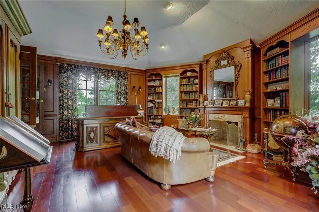 Living area featuring lofted ceiling, a chandelier, dark wood-style flooring, a high end fireplace, and built in shelves