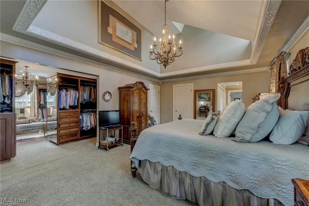 Bedroom featuring a raised ceiling, a chandelier, a closet, ornamental molding, and carpet