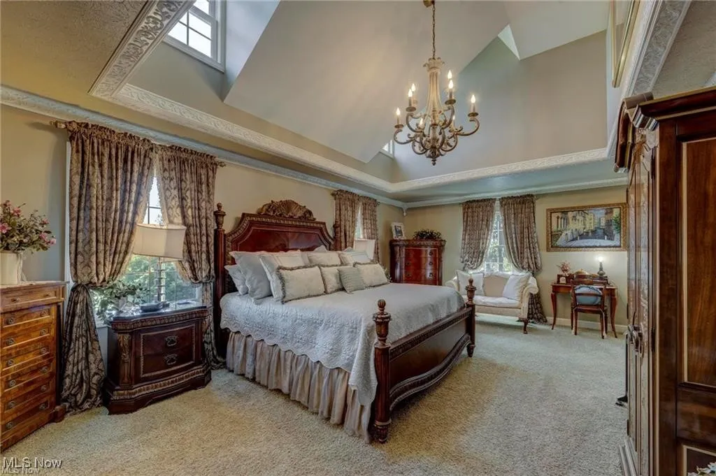 Bedroom with light carpet, a tray ceiling, high vaulted ceiling, and a chandelier