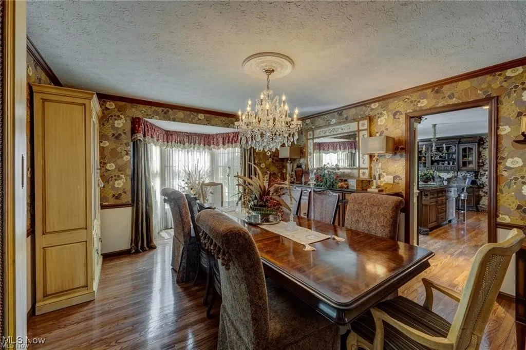 Dining room with wallpapered walls, a textured ceiling, wood finished floors, a chandelier, and crown molding