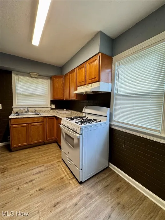 Kitchen featuring white gas range oven, under cabinet range hood, brown cabinetry, and light wood-style floors