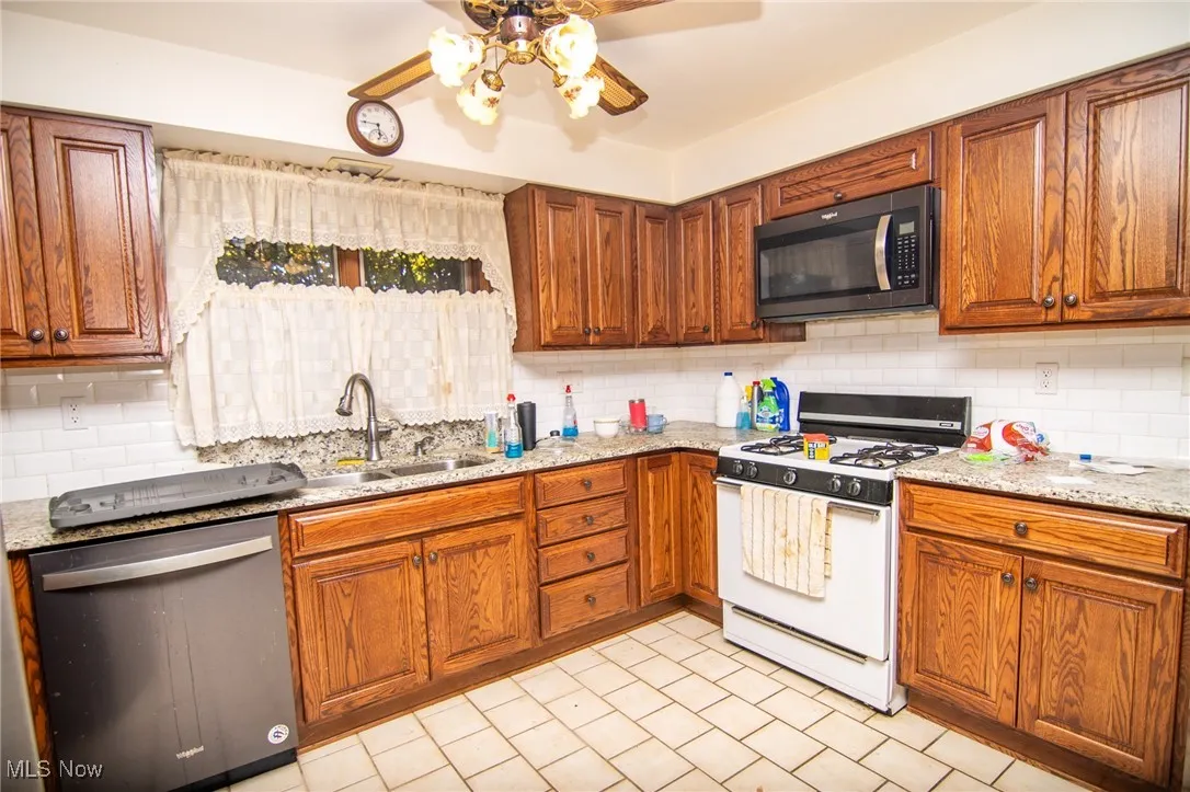Kitchen with white gas range, brown cabinets, decorative backsplash, and stainless steel dishwasher