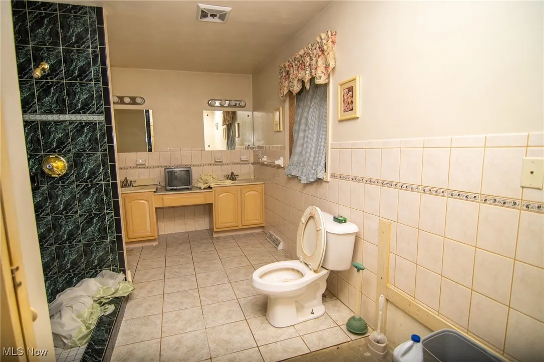 Full bath featuring light tile patterned flooring, tile walls, vanity, a wainscoted wall, and a shower with shower curtain