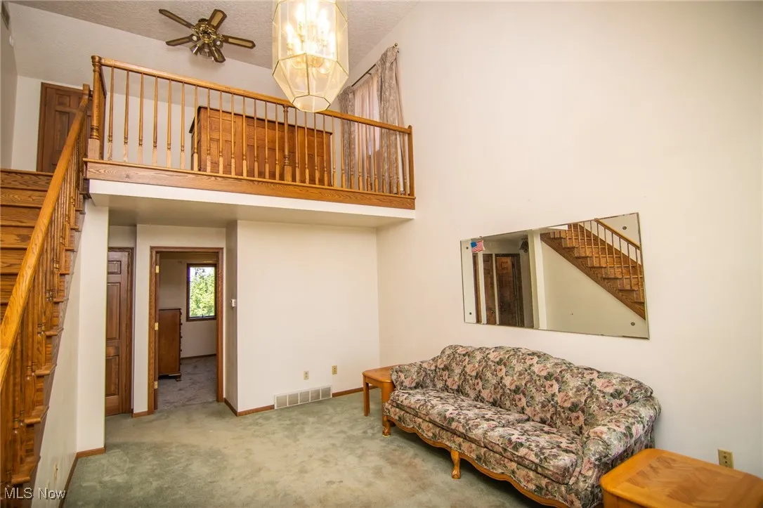 Sitting room featuring stairs, carpet flooring, a high ceiling, a textured ceiling, and a ceiling fan