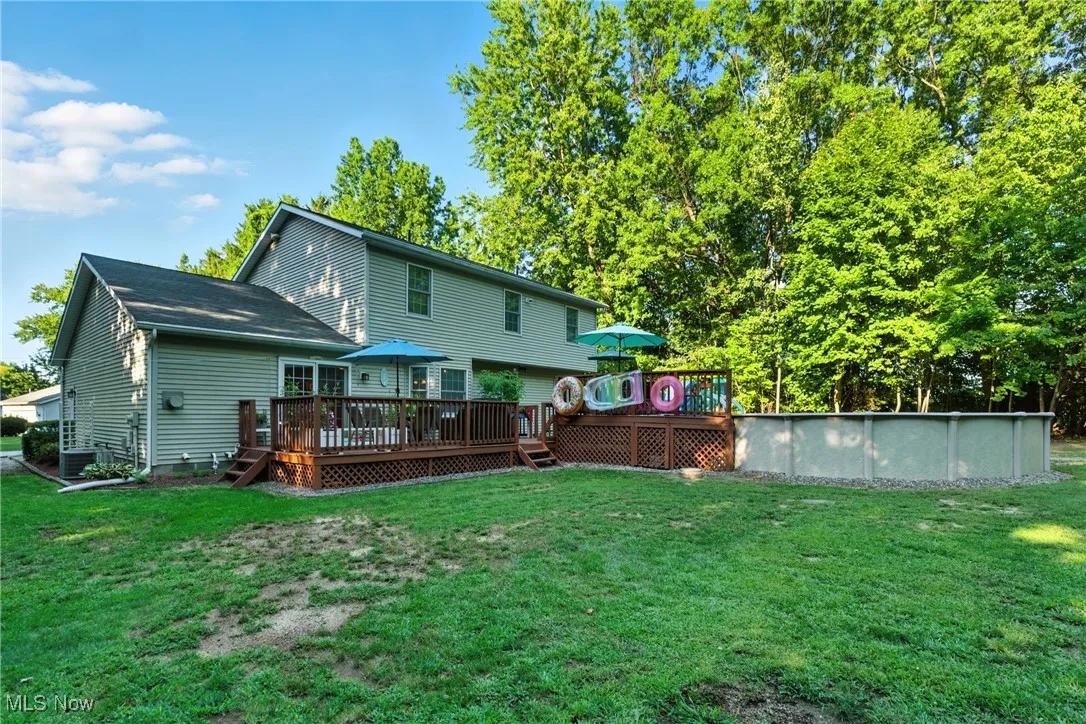 Rear view of property with a wooden deck, a lawn, and an outdoor pool