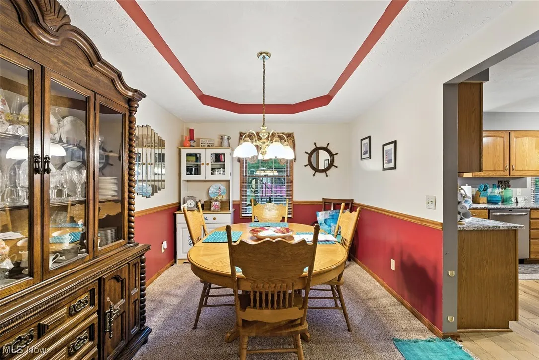 Dining space featuring a tray ceiling, a chandelier, light carpet, a textured ceiling, and light wood-style floors