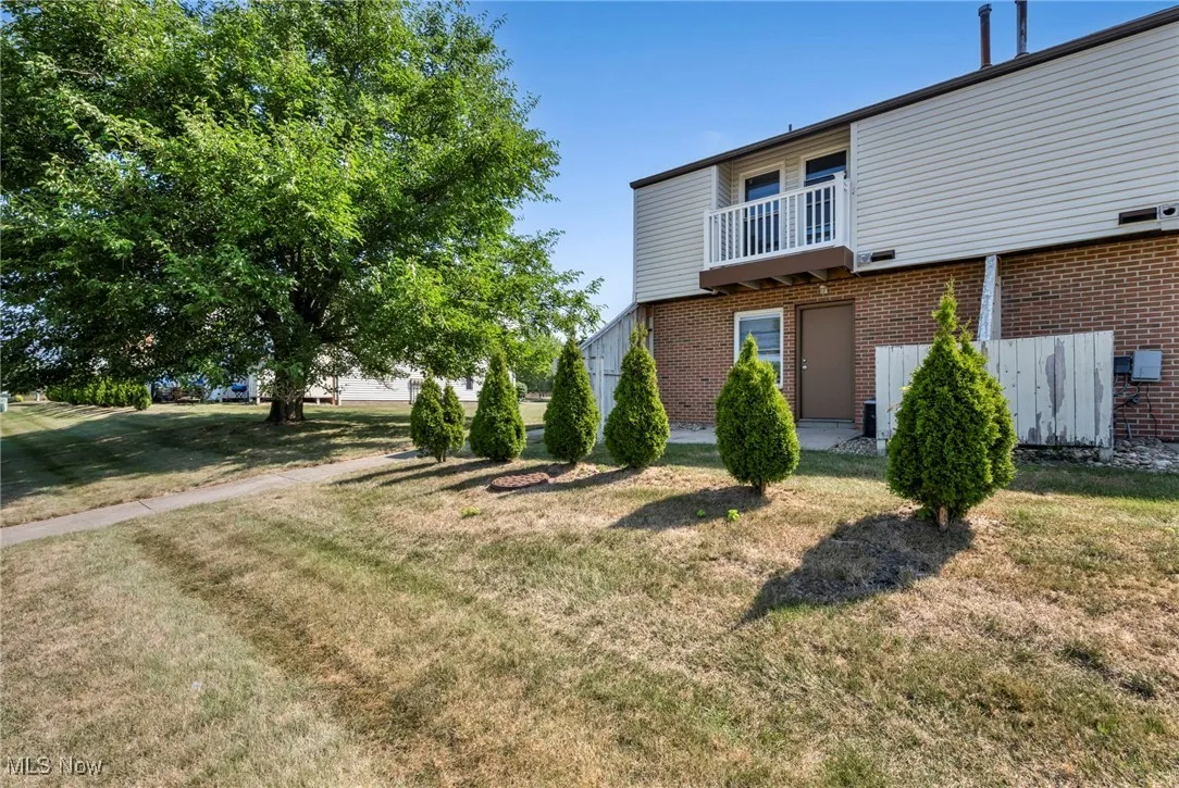 Back of house featuring a balcony, brick siding, and a yard