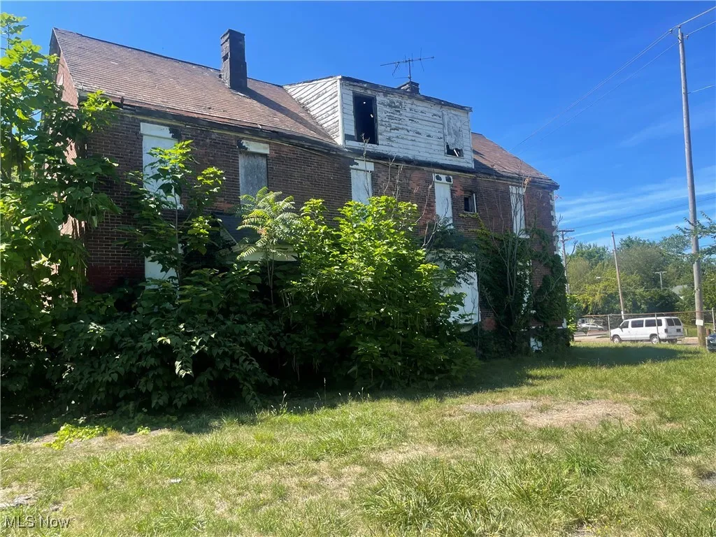 Rear view of house with brick siding, a chimney, and a yard