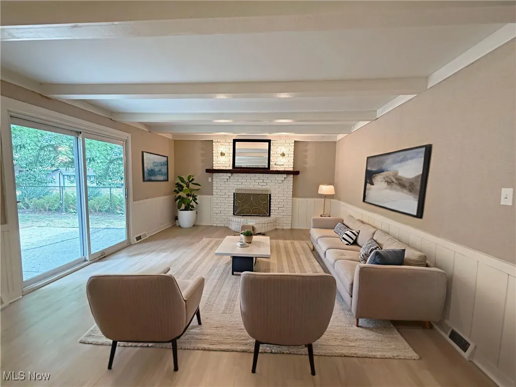Living area with a wainscoted wall, a decorative wall, light wood-style flooring, beam ceiling, and a fireplace