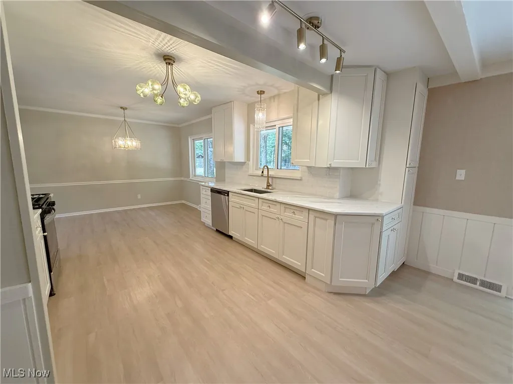 Kitchen featuring tasteful backsplash, white cabinetry, light wood-style flooring, appliances with stainless steel finishes, and ornamental molding