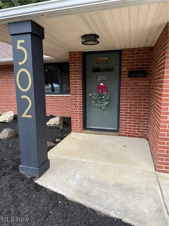 Doorway to property with brick siding and a porch
