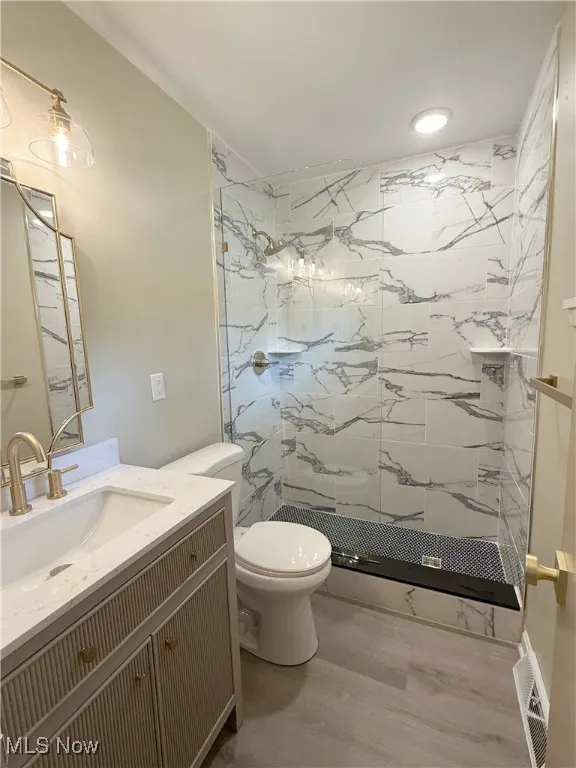 Bathroom featuring vanity, a marble finish shower, and light wood-type flooring