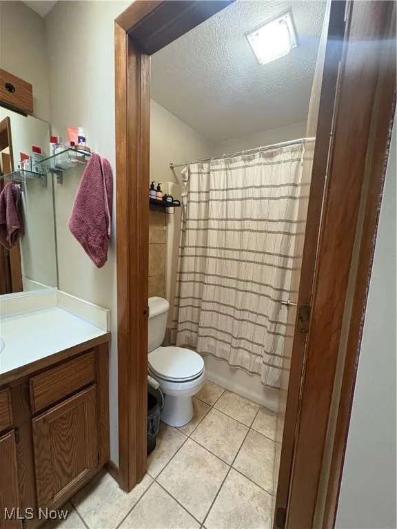 Master bathroom with a textured ceiling, vanity, light tile patterned floors, and shower / bathtub combination with curtain skylight