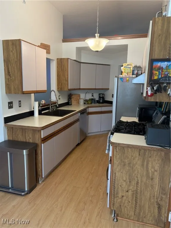 Kitchen featuring brown cabinets, hanging light fixtures, light wood-type flooring, light countertops, and black dishwasher