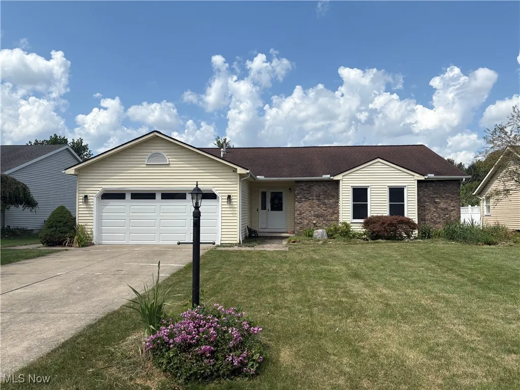 Ranch-style house featuring an attached garage, concrete driveway, brick siding, a front yard, and a shingled roof
